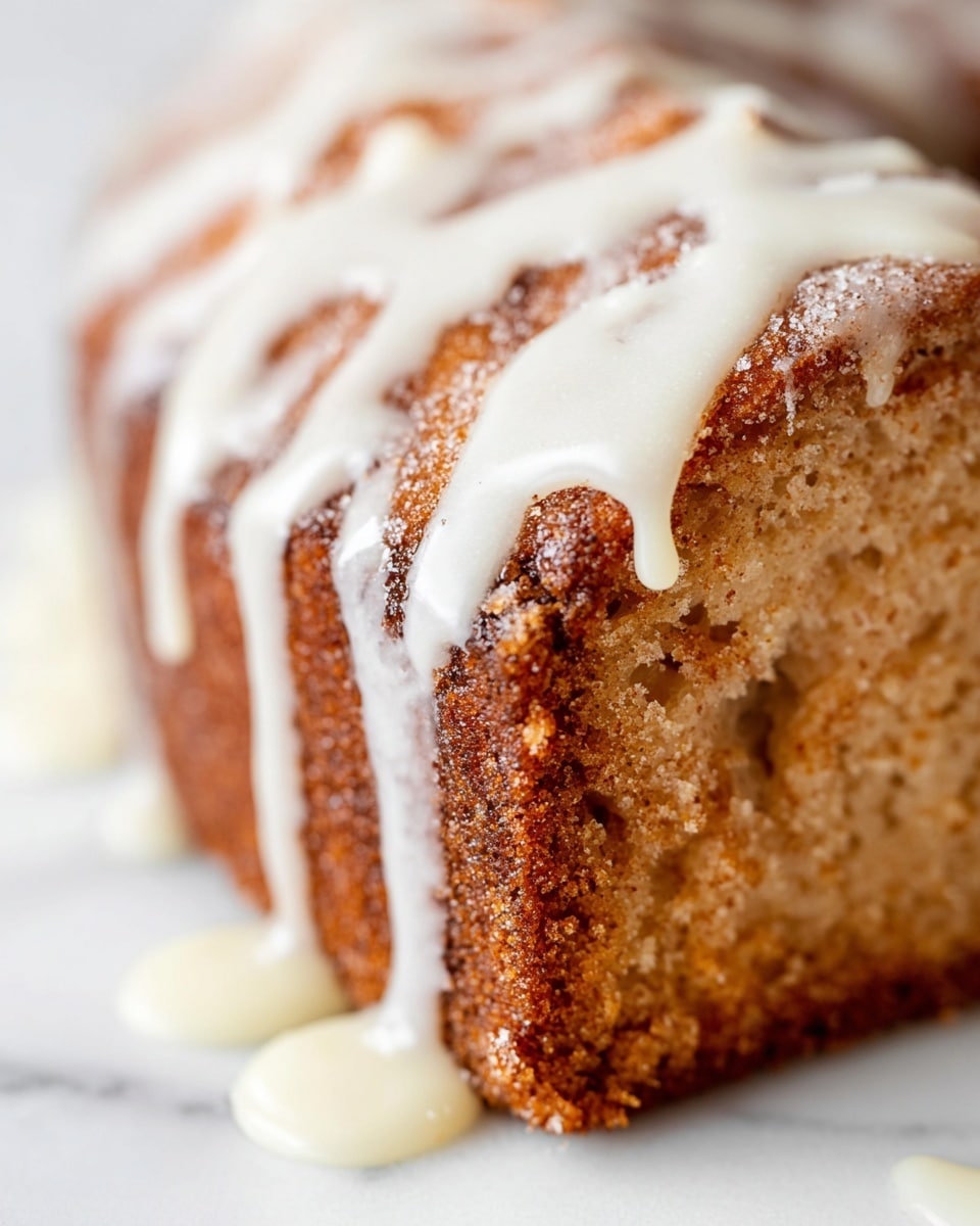A close-up view of a single thick slice of a cinnamon sugar cake shows a golden-brown crumbly texture covered unevenly by a smooth, shiny white glaze that drips down the sides and pools slightly at the base. The cake's surface has a rough, grainy texture from the cinnamon sugar blend, with visible cracks and crevices. The white glaze contrasts sharply against the warm, toasted brown colors of the cake, creating a visually appealing layer on top. The background is a white marbled texture. photo taken with an iphone --ar 4:5 --v 7