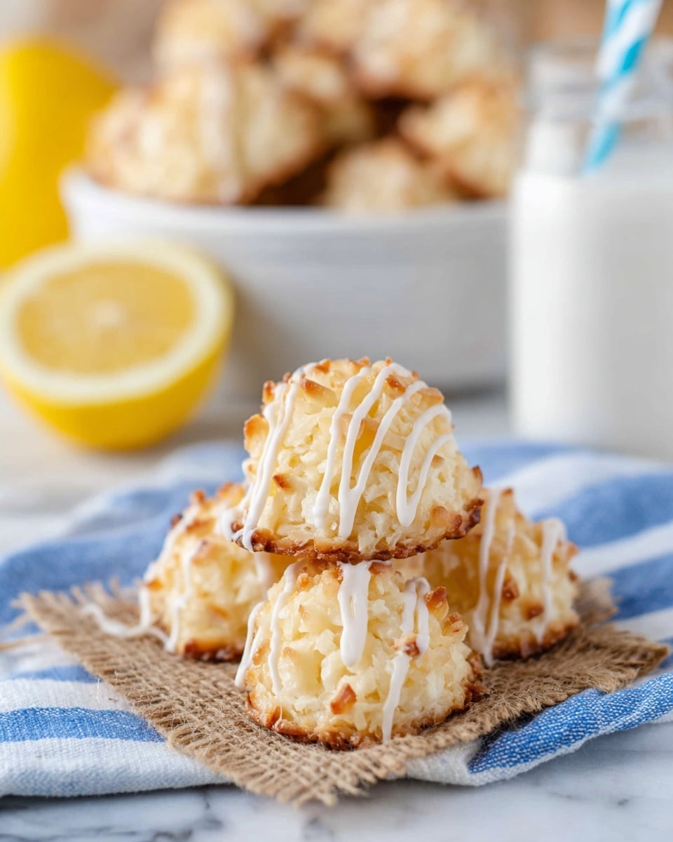 The image shows a small pile of four light golden toasted coconut macaroons with a rough, textured surface. Each macaroon is topped with thin, white icing drizzled in vertical lines. They rest on a piece of coarse brown fabric over a white cloth with blue stripes, placed on a white marbled surface. In the background, there is a slightly out-of-focus white bowl filled with more macaroons, a half-cut lemon, and a glass jar of milk with a blue and white striped straw. photo taken with an iphone --ar 4:5 --v 7