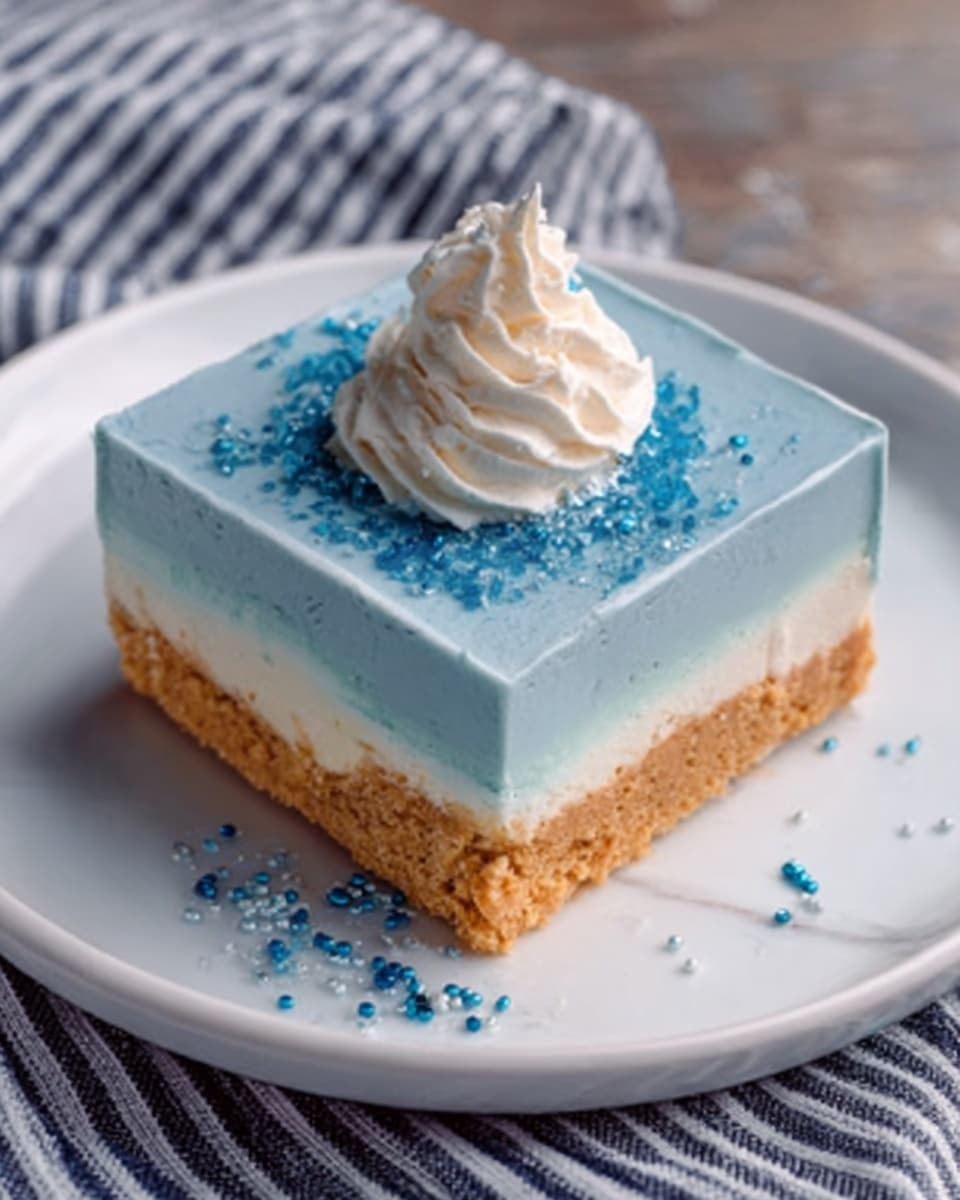 A square dessert with three clear layers sits on a white plate. The bottom layer is thick and golden brown with a crumbly texture, likely a crust. Above it is a thicker, smooth, light blue layer that looks creamy. The top has a small swirl of whipped cream in the center, decorated with small blue sprinkles scattered around it. The plate is set on a white marbled surface with a striped towel nearby. The scene looks bright and clean, with natural light highlighting the dessert’s colors and layers. Photo taken with an iphone --ar 4:5 --v 7