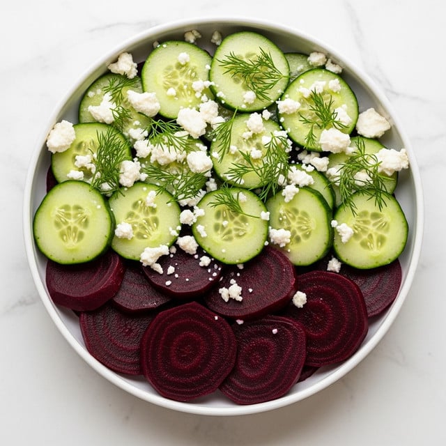 A white bowl filled with a layered salad on a white marbled surface, showing the bottom layer of deep purple beet slices with a smooth texture, topped with bright green cucumber slices that have pale centers and a slightly ridged edge; scattered on top are crumbled white cheese pieces and fresh green dill sprigs that add a feathery texture and contrast of colors. Photo taken with an iphone --ar 4:5 --v 7