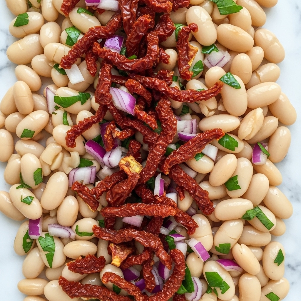 The image shows a close view of a bean salad with three main layers visible: the base layer of smooth, plump white beans, each one oval and shiny; scattered chopped pieces of dried tomato in a dark red, slightly wrinkled texture are layered evenly among the beans; and small bits of fresh green herbs and purple onion pieces add vibrant color throughout. The elements are mixed closely together with a light coating of oil or dressing, making the beans look glossy. The background is a white marbled texture. photo taken with an iphone --ar 4:5 --v 7